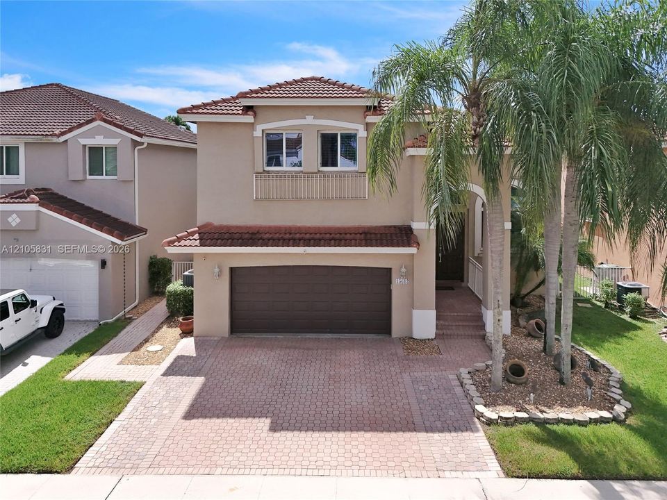 Two-story exterior featuring a stucco facade, red tile roof, two-car garage, and a brick-paver driveway