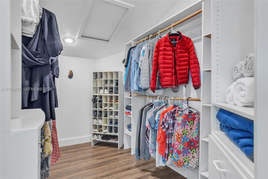 Walk-in closet featuring white built-in shelving, integrated shoe cubbies, wood-finish flooring, and recessed lighting