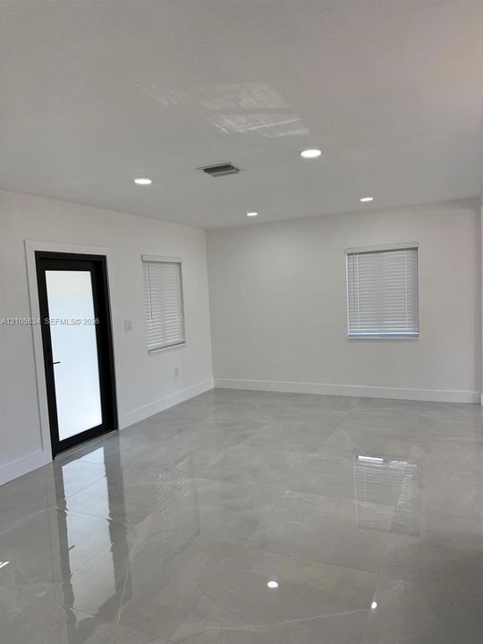 Large-format tile flooring, recessed ceiling lighting, and a glass-paneled exterior door with a dark frame