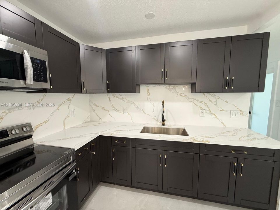 Kitchen featuring dark shaker-style cabinetry, quartz countertops with integrated backsplash, stainless steel undermount sink, matte black hardware, and stainless steel appliances