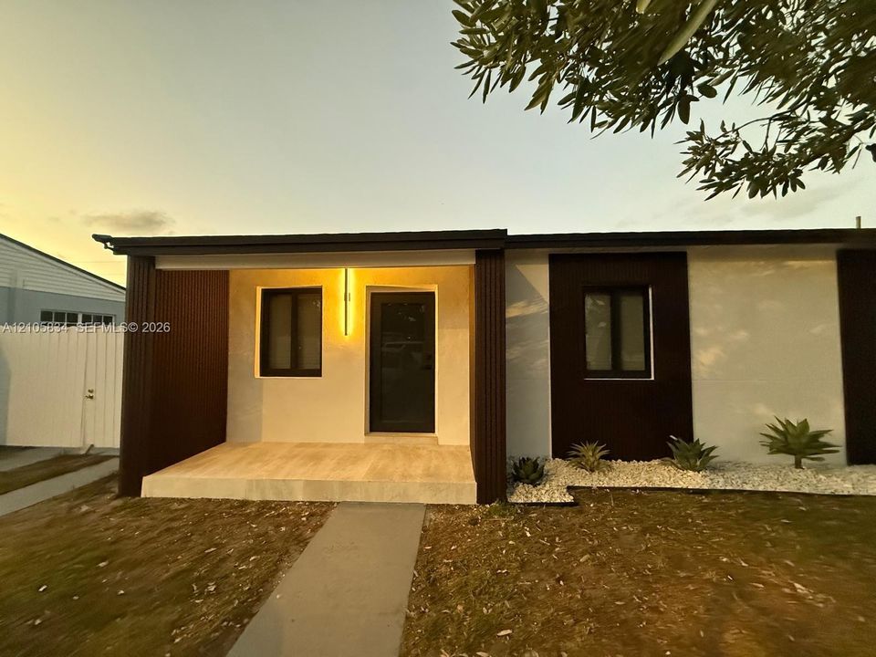 Modern facade featuring high-contrast white and dark-toned paneling, a covered front entryway, stone-tiled porch, and low-maintenance xeriscaped front garden beds