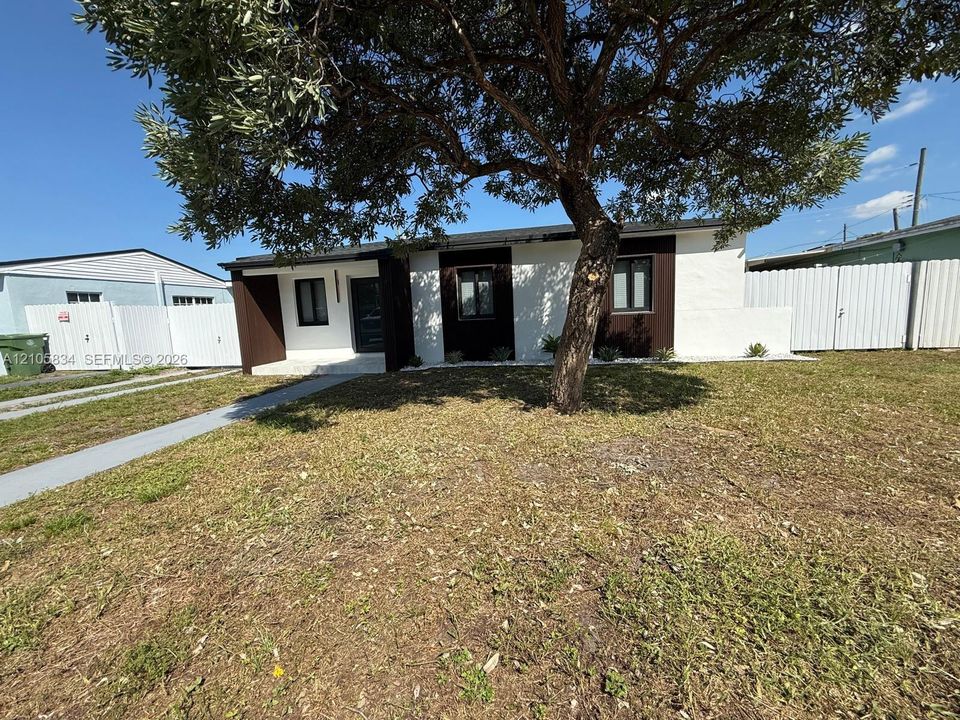 Exterior facade featuring white stucco walls with dark wood-finish paneling, a concrete walkway, and white vinyl privacy fencing