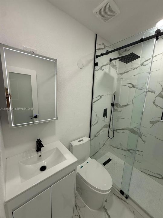 Bathroom featuring a vanity with an integrated sink, matte black faucet, and LED-backlit mirror