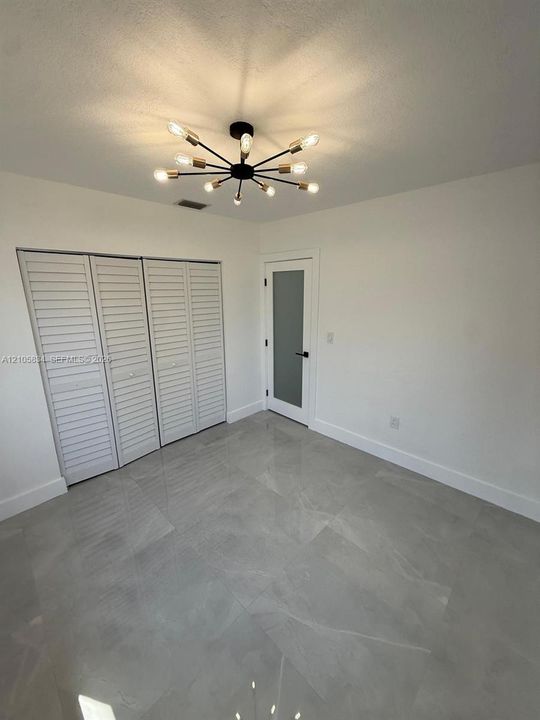 Polished large-format tile flooring, modern multi-arm sputnik chandelier, tri-fold louvered closet doors, and single-panel door with frosted glass insert