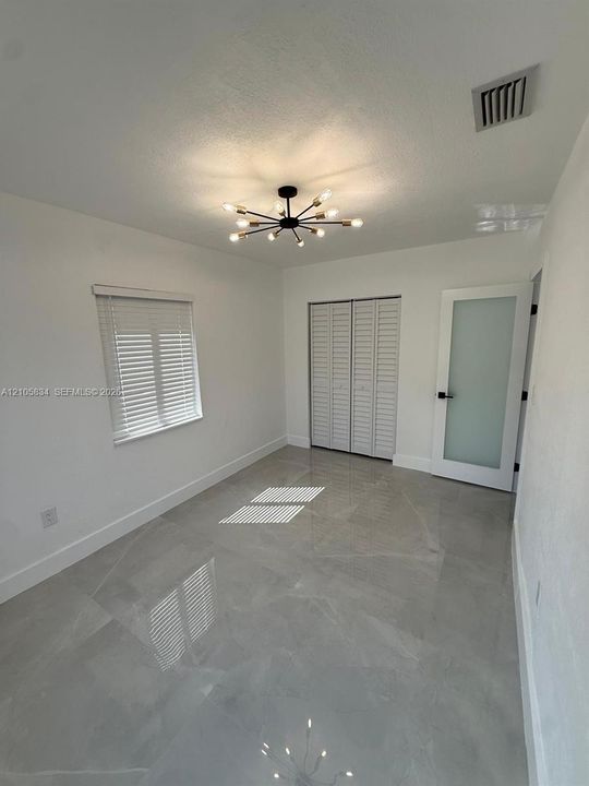 Large-format tile flooring, modern multi-arm sputnik chandelier, frosted glass panel door with matte black hardware, and bi-fold louvered closet doors