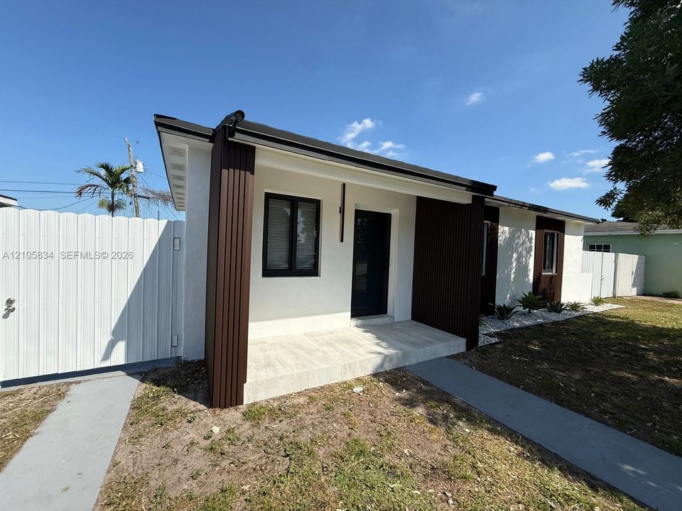 Exterior facade featuring white stucco finish, vertical dark-toned siding accents, a covered concrete entryway, and solid white privacy fencing