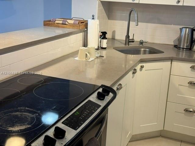 Kitchen featuring white shaker-style cabinetry, neutral-toned solid surface countertops, subway tile backsplash, stainless steel drop-in sink with a high-arch pull-down faucet, and a glass-top electric range