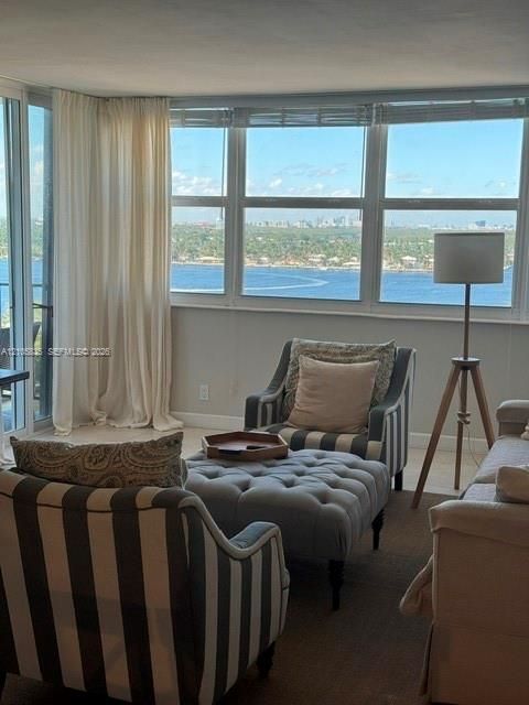 Floor-to-ceiling windows featuring panoramic water and cityscape scenery, sliding glass door with access to a balcony, and neutral tile flooring