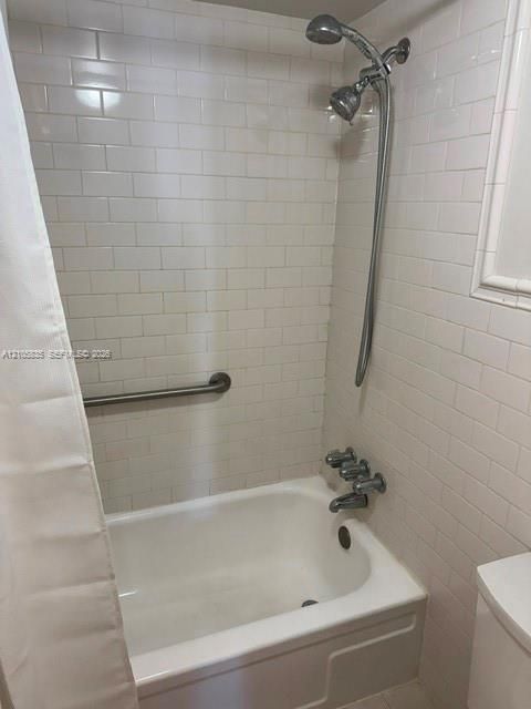 Bathtub and shower combination featuring white subway tile surround, polished chrome fixtures, and wall-mounted grab bar