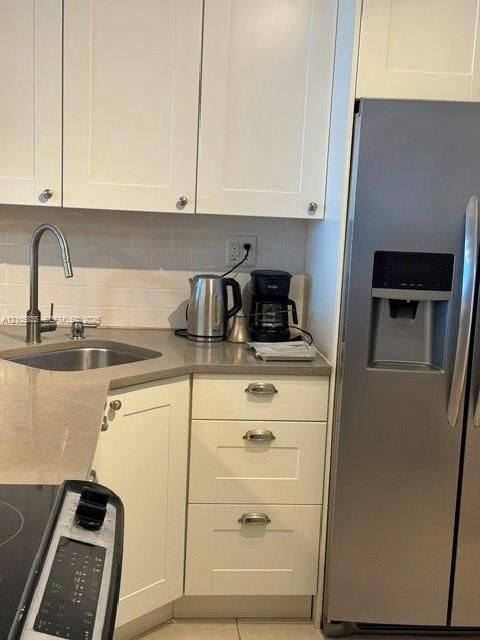 Shaker-style white cabinetry, stone-finish countertops, stainless steel side-by-side refrigerator, under-mount stainless steel sink, and arched-neck faucet