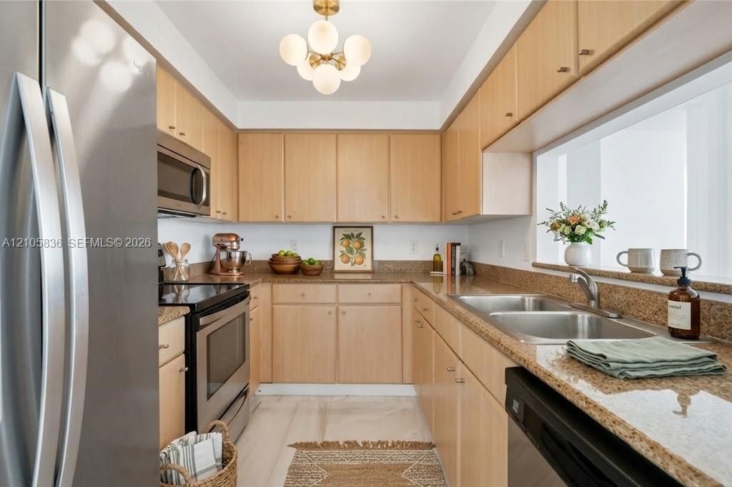 Kitchen featuring light wood cabinetry, stone countertops, stainless steel appliances, a double-basin undermount sink, and a multi-globe light fixture