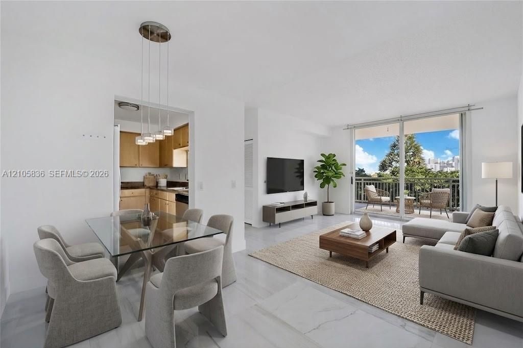 Open-concept living area featuring light-toned flooring, sliding glass doors to a private balcony, and a multi-light pendant fixture above the dining area