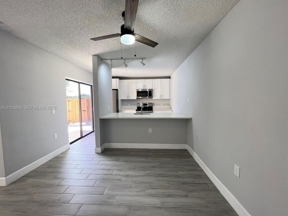 Kitchen featuring white cabinetry, stainless steel appliances, a peninsula counter with a sink, wood-finish tile flooring, and a ceiling fan with integrated lighting