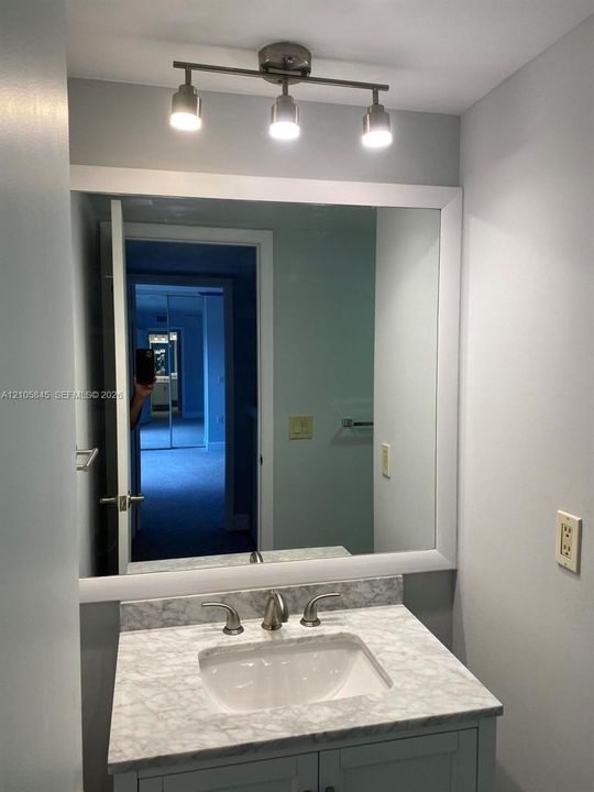 Vanity featuring a stone-look countertop, integrated rectangular sink, widespread metallic faucet, framed wall mirror, and three-light track fixture