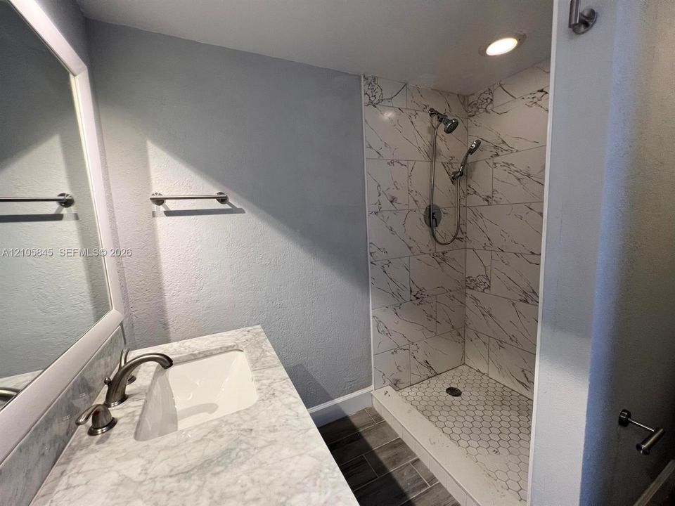 Bathroom featuring a vanity with a stone-top counter, undermount sink, and metallic faucet, paired with a walk-in shower showcasing large-format wall tile, hexagonal floor tile, and a multi-head shower system