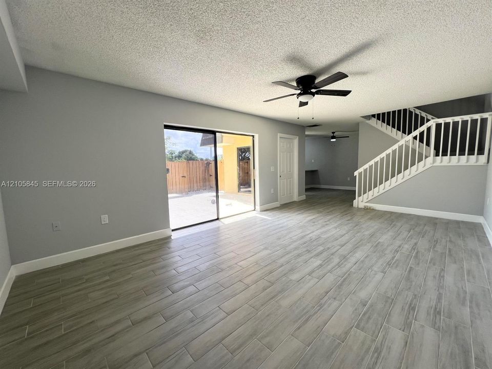 Open-concept interior featuring wood-finish tile flooring, a sliding glass door, white stair railing, and a ceiling fan