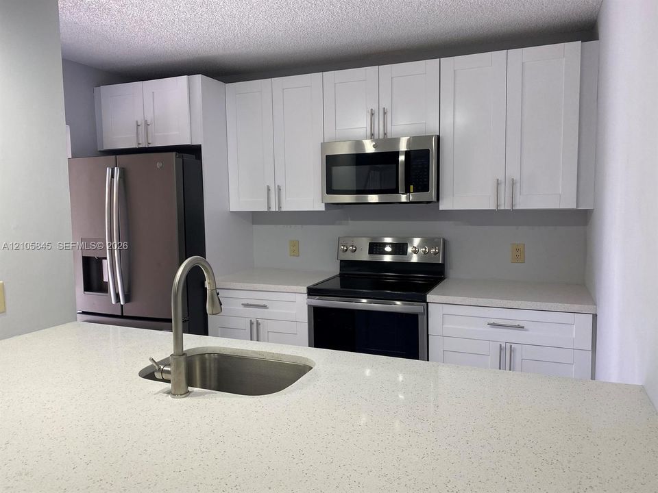 Kitchen featuring white shaker-style cabinetry, solid-surface countertops, stainless steel appliances, and an undermount sink with a high-arch pull-down faucet