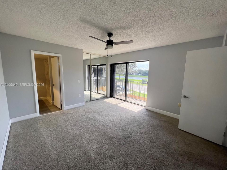 Neutral-toned interior featuring wall-to-wall carpeting, mirrored closet doors, a ceiling fan with integrated lighting, and a sliding glass door opening to an exterior balcony