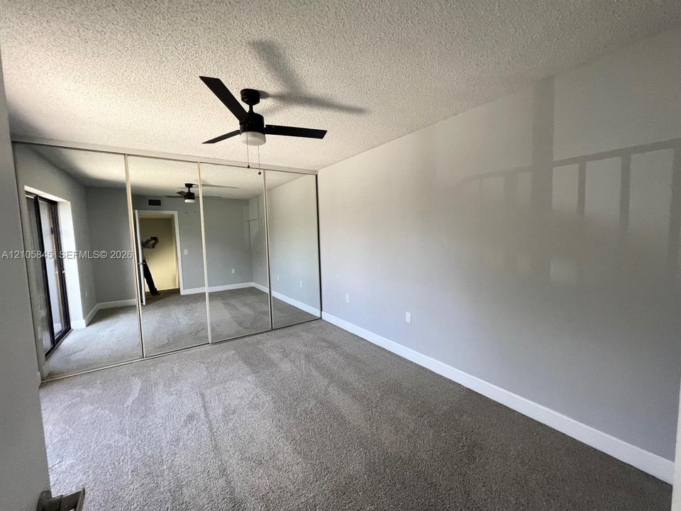 Room featuring wall-to-wall mirrored sliding closet doors, neutral carpeting, and a ceiling fan with integrated lighting