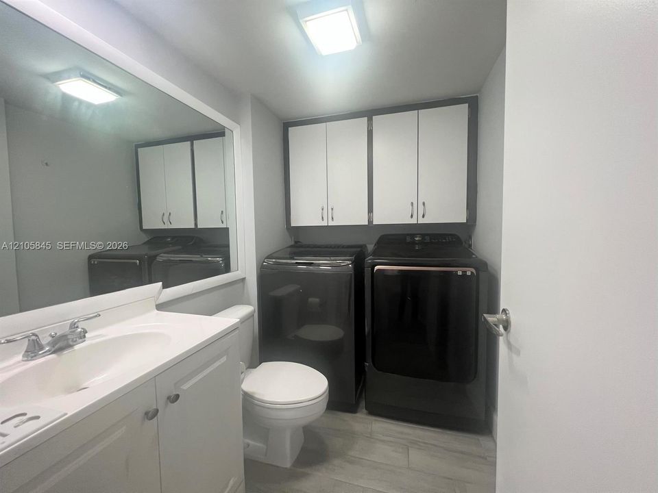 Bathroom featuring white cabinetry, integrated sink, large wall-mounted mirror, overhead lighting, and wood-finish tile flooring