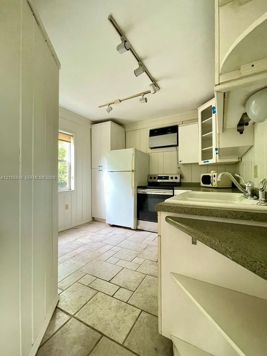Kitchen featuring tile flooring, white cabinetry, integrated track lighting, and a composite countertop with an inset sink