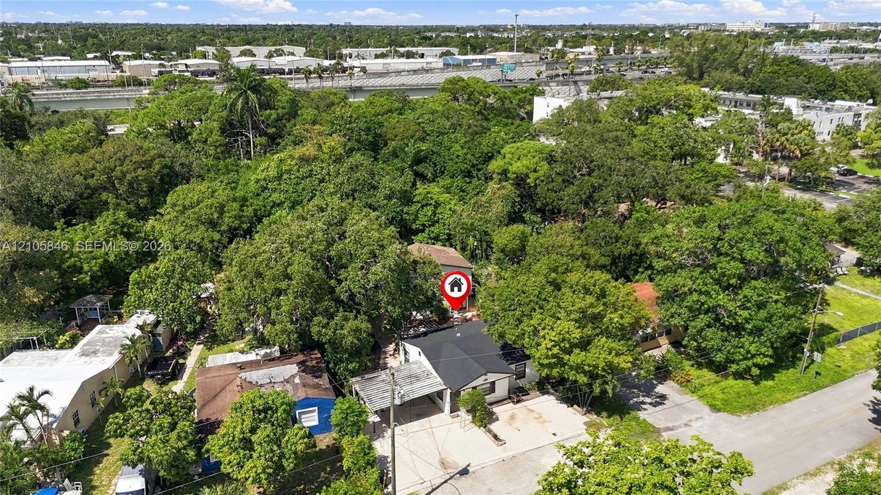 Aerial perspective of a detached residence featuring a paved driveway, covered entryway, pitched shingle roof, and mature tree canopy