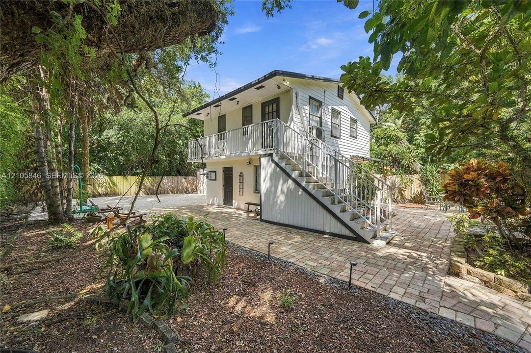 Two-story detached structure featuring horizontal siding, exterior staircase with metal railing, upper-level balcony, and a paved brick patio