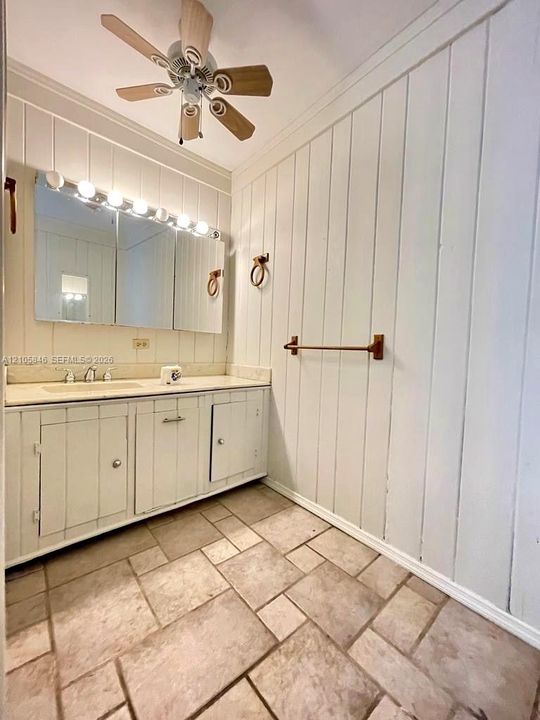 Vertical paneled walls, stone-tiled flooring, custom cabinetry with an integrated countertop, multi-bulb lighting fixture, and metallic hardware