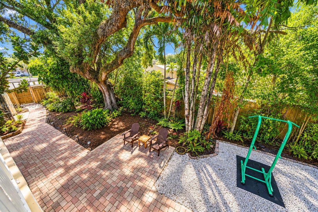 Landscaped backyard featuring paver patio, gravel ground cover, mature trees, and wooden perimeter fencing
