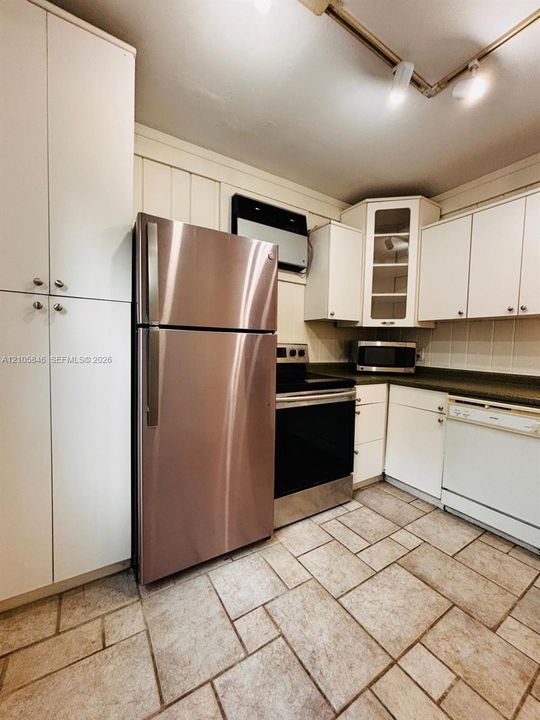 Kitchen featuring white cabinetry with glass-panel accents, stainless steel refrigerator, dark solid-surface countertops, and tile flooring