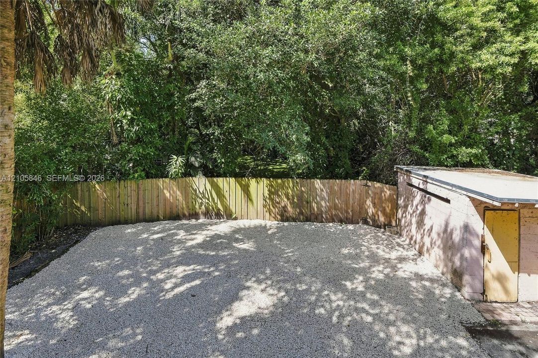 Gravel-surfaced yard featuring a wood fence enclosure and mature perimeter trees