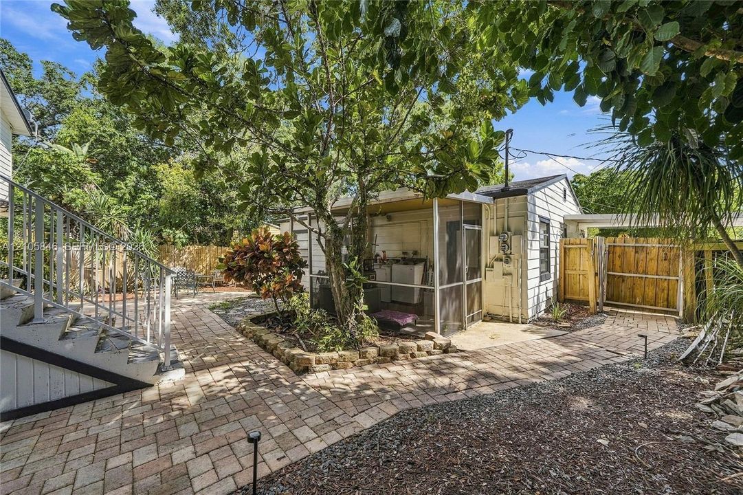 Exterior grounds featuring brick paver hardscaping, a screened-in porch, metal staircase with railings, wood fencing, and mature landscaping