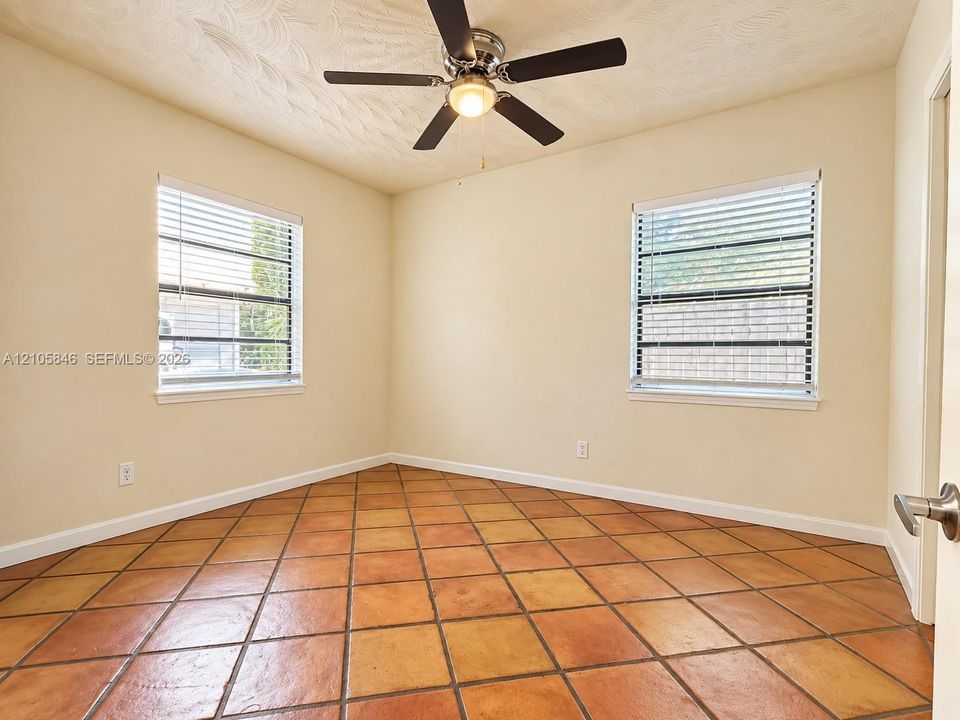 Interior room featuring large-format terra cotta tile flooring, dual windows with integrated blinds, and a centrally mounted ceiling fan with light fixture