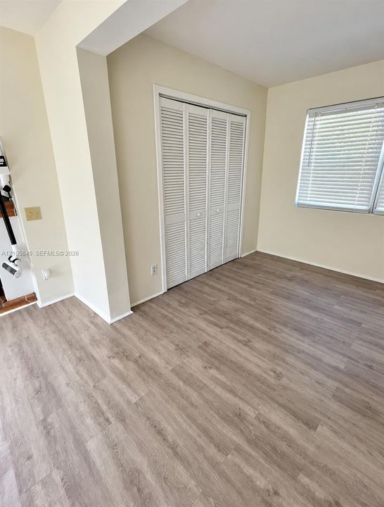 Neutral-toned walls, wood-finish flooring, and white louvered bifold closet doors, complemented by a window with horizontal blinds