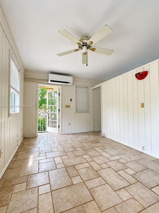 Vertical tongue-and-groove wall paneling, modular tile flooring, wall-mounted ductless HVAC unit, ceiling fan with light fixture, and multi-pane glass door