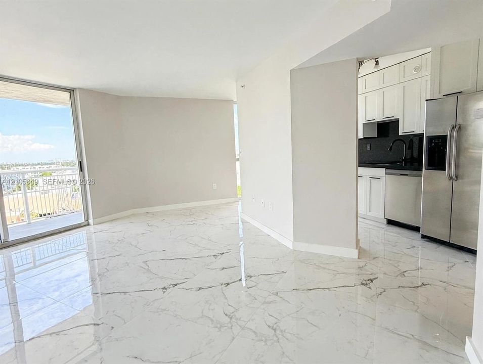Large-format tiled flooring with veined detailing, white cabinetry, stainless steel appliances, and sliding glass door access to an exterior balcony