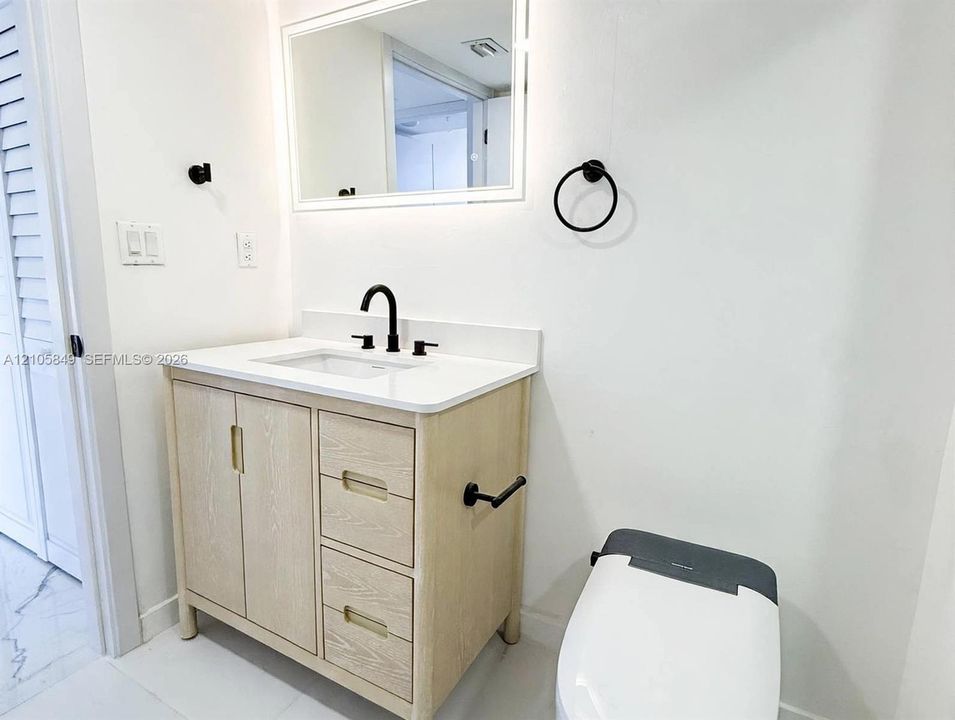 Light wood-finish vanity with a white countertop, rectangular undermount sink, matte black faucet, and an integrated backlit mirror