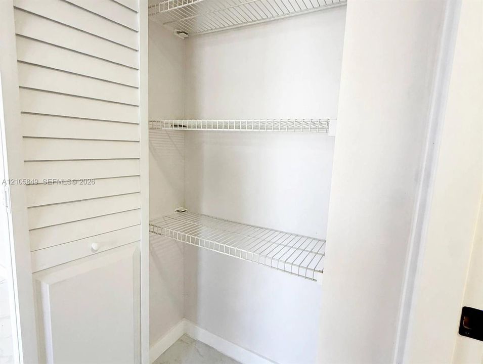 Storage closet featuring white louvered double doors and interior white wire shelving