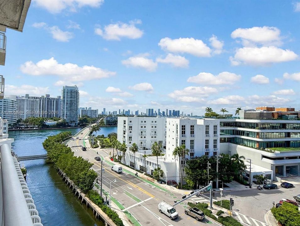 Elevated balcony featuring a metal railing, overlooking urban skyline, water channel, and infrastructure