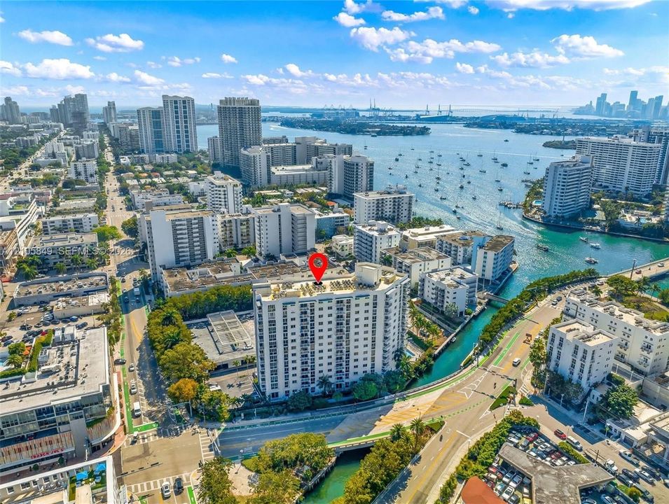 Aerial perspective of mid-rise residential building featuring a rooftop pool, private surface parking, and proximity to the waterfront