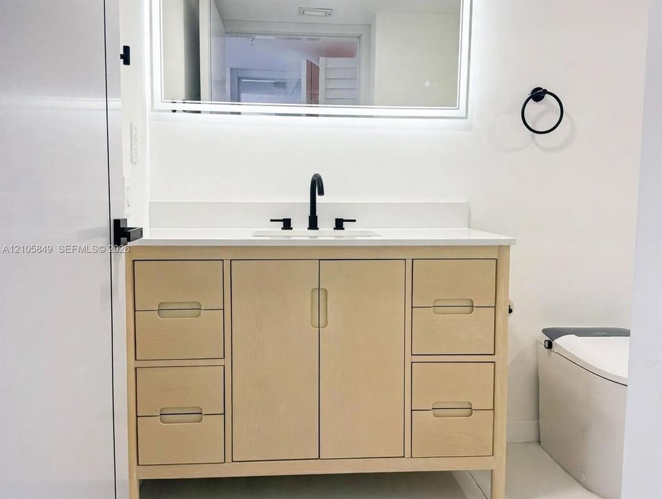 Light-toned wood vanity with integrated storage drawers and cabinets, topped with a solid-surface countertop and undermount sink