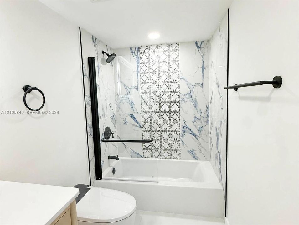 Bathtub with floor-to-ceiling marbled wall tile and decorative geometric tile inlay, complemented by matte black fixtures including a wall-mounted towel bar and circular ring