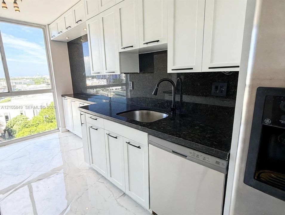 White Shaker cabinetry with matte black hardware, dark stone countertops, full-height stone backsplash, stainless steel undermount sink with a gooseneck faucet, and polished large-format tile flooring