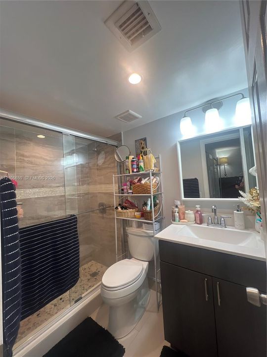 Bathroom featuring a dark-finish vanity with a white countertop and integrated sink, a glass-enclosed shower with tiled walls, and three-light wall-mounted vanity lighting