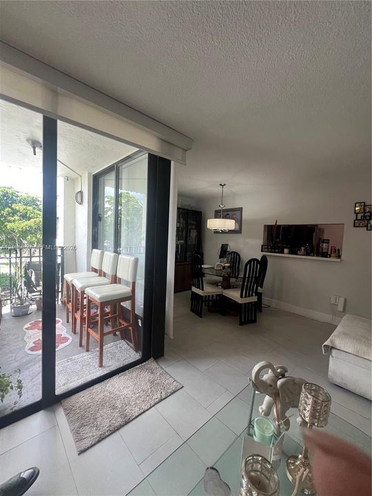 Interior space featuring large format light-toned tile flooring, oversized glass sliding doors, a built-in pass-through wall opening, and a hanging drum-style light fixture