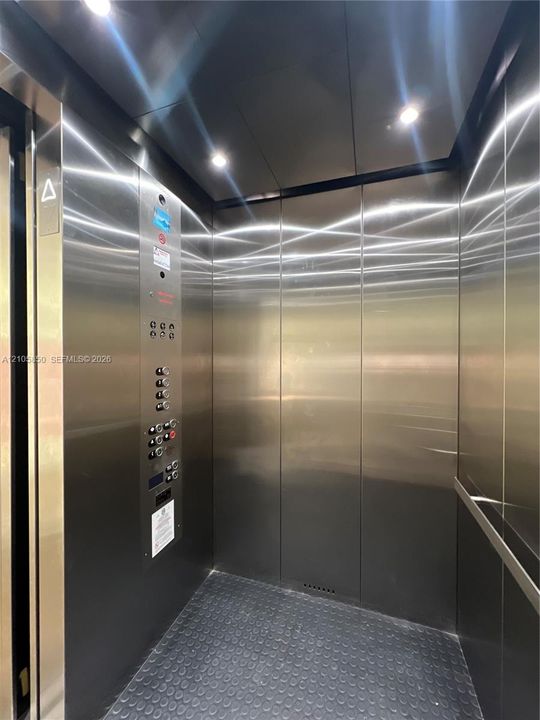 Elevator interior featuring brushed stainless steel paneling, recessed ceiling lighting, a textured rubberized floor, and an integrated control panel