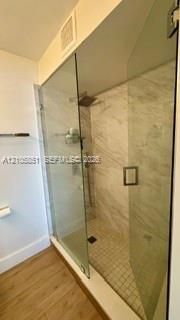 Walk-in shower featuring a frameless glass enclosure, stone-finish wall tile, a rain-style showerhead, a hand-held shower wand, and a mosaic-tile floor