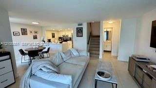 Open-concept interior featuring large-format tile flooring, recessed lighting, white cabinetry, neutral wall paint, and a built-in staircase with a wooden handrail