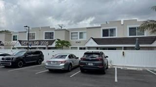 Multi-unit exterior featuring a neutral stucco facade, tiered parapet rooflines, dark-toned tile roofing, and white privacy fencing