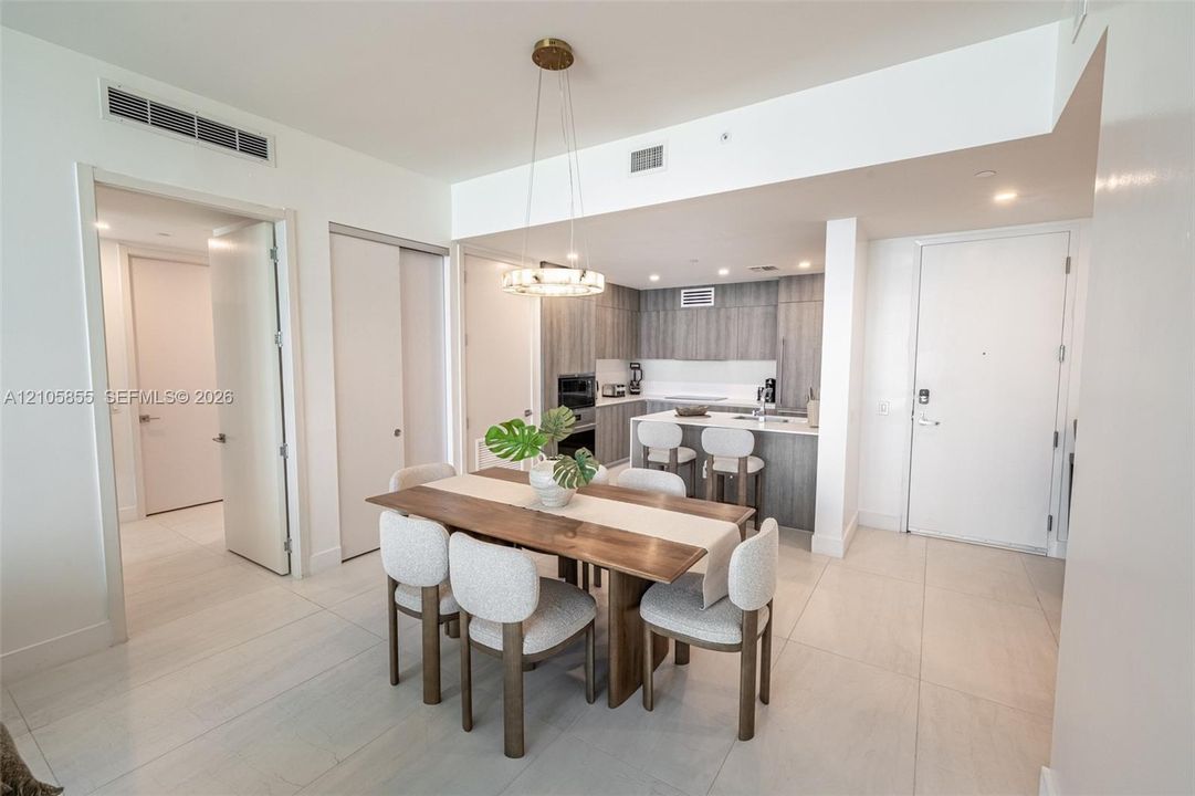 Kitchen featuring flat-panel cabinetry, light-toned countertops, a breakfast bar, and stainless steel appliances, highlighted by a contemporary circular pendant light fixture and consistent tile flooring
